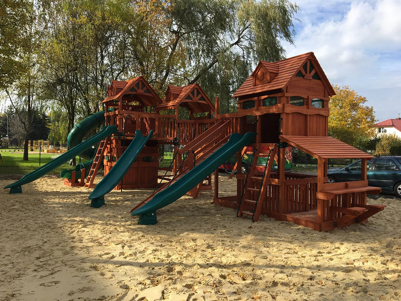 Estructura de parque infantil de madera con toboganes y zona de arena en un entorno de parque